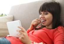 En ung kvinde ligger på en sofa og holder en tablet i hånden. Hun er iført en rød trøje og ser ud til at være afslappet.