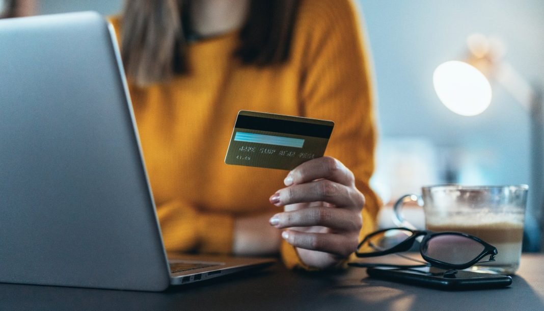 shein-wallet Pigen foran en bærbare computer med et kreditkort i hånden.