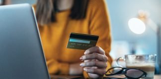 Pigen foran en bærbare computer med et kreditkort i hånden.