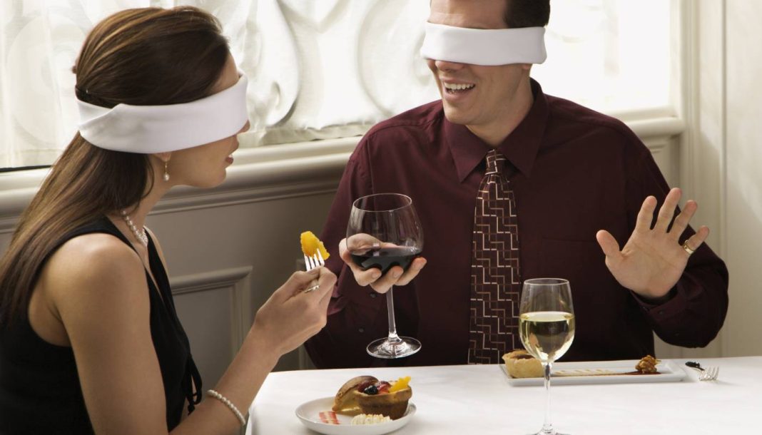 En mand og en kvinde drikker vin ved et bord med bind for øjnene.