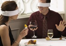Sådan spotter og undgår du en online dating-svindler: 9 røde flag En mand og en kvinde drikker vin ved et bord med bind for øjnene.