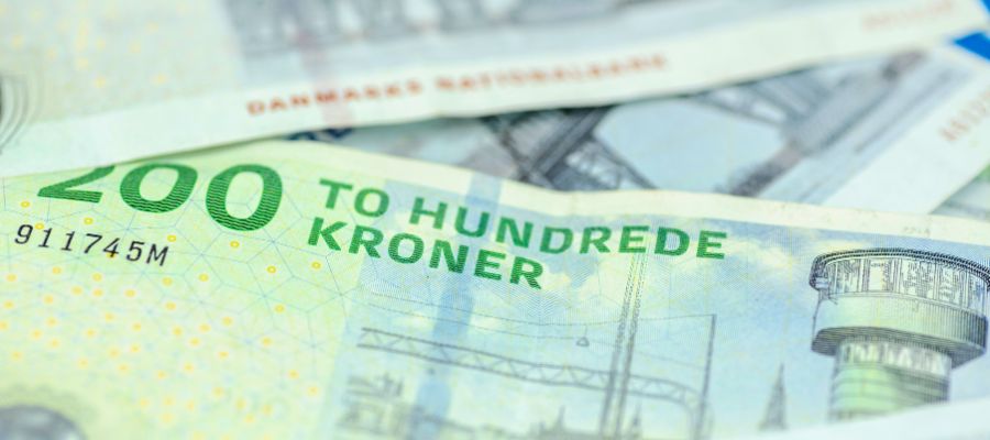 Et nærbillede af en dansk 200-kroneseddel, hvorpå teksten "TO HUNDREDE KRONER" er tydeligt synlig i grøn skrift. Dele af et arkitektonisk motiv kan anes i baggrunden, og der ligger andre sedler sløret underneden.