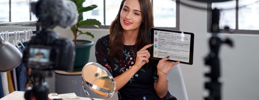 En bloggerpige sidder foran kameraet med en tablet i hænderne.