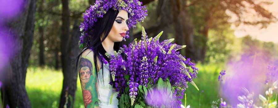 Pigemodel i skov med buket af lilla blomster og krans på hovedet lavet af lilla blomster
