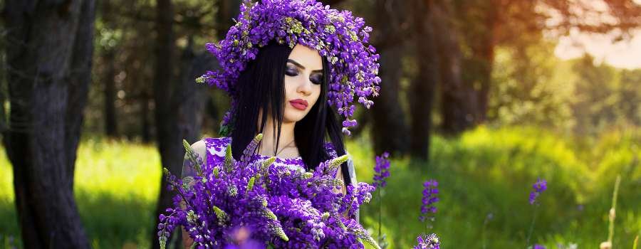 Pigemodel i skov med buket af lilla blomster og krans på hovedet lavet af lilla blomster