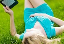 En lyshåret pige med en e-bog i hænderne ligger på græsset