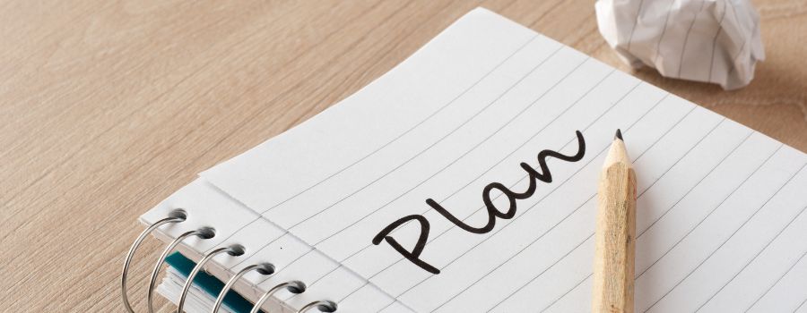 På bordet ligger en notesbog, hvor der står "Plan".