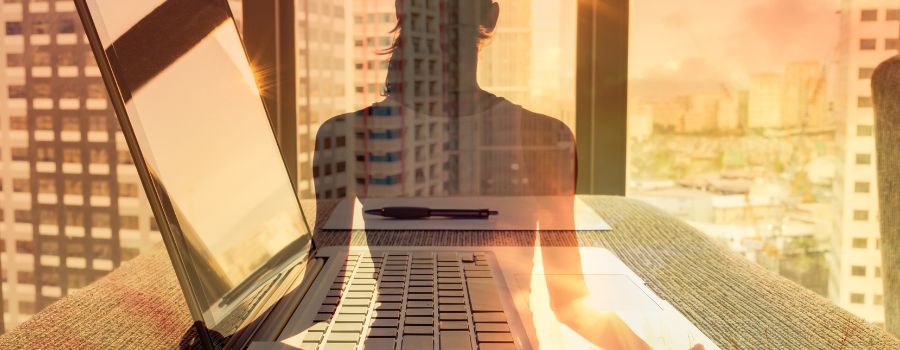 En laptop står på et bord med den gennemsigtige skygge af en pige med høretelefoner i forgrunden