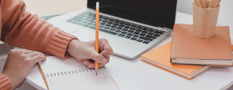 En pige ved et skrivebord med en blyant i hånden og en åben notesbog.