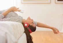 En pige med høretelefoner ligger på sengen.