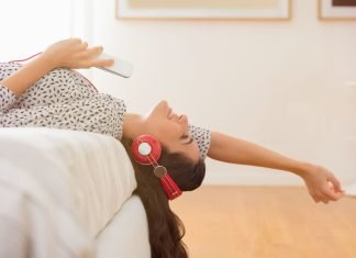 En pige med høretelefoner ligger på sengen.