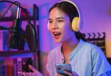 En pige iført høretelefoner og med en telefon i hånden foran en mikrofon med åben mund