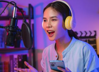 En pige iført høretelefoner og med en telefon i hånden foran en mikrofon med åben mund