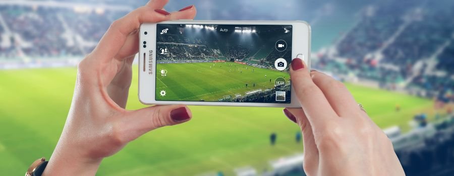 Pige tager billeder af sportsstadion med hvid samsung-smartphone.