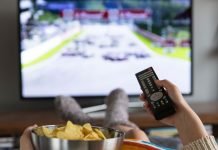 En pige med en skål popcorn og en fjernbetjening i hånden sidder foran fjernsynet