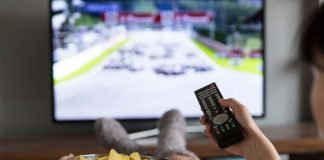 En pige med en skål popcorn og en fjernbetjening i hånden sidder foran fjernsynet