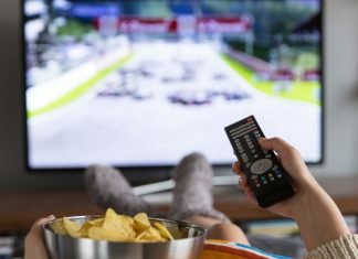 En pige med en skål popcorn og en fjernbetjening i hånden sidder foran fjernsynet