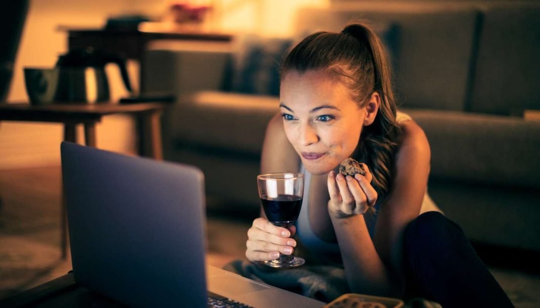 En pige med et glas vin sidder i en sofa foran en bærbar computer