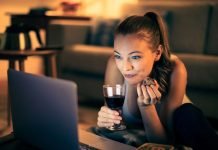 En pige med et glas vin sidder i en sofa foran en bærbar computer