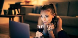 En pige med et glas vin sidder i en sofa foran en bærbar computer