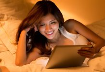 Asiatisk pige med en tablet i hænderne ligger i sengen