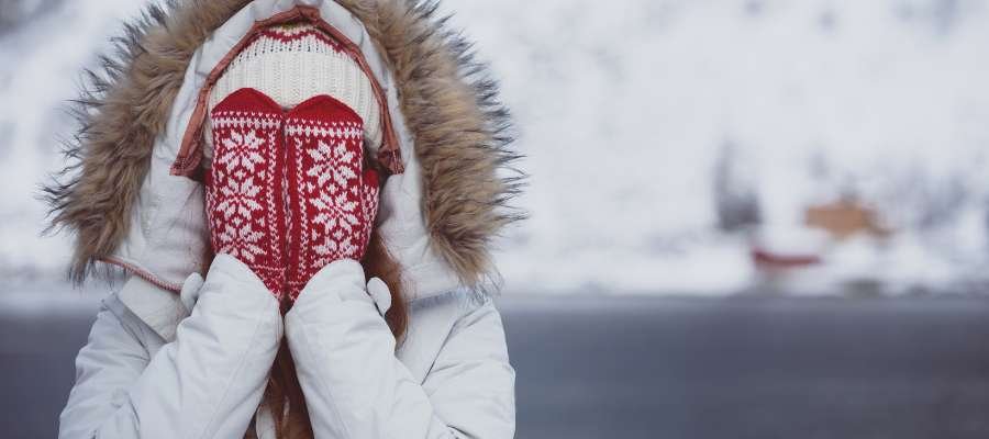 Pigen i en hue og vinterjakke dækker sit ansigt med hænderne i vanter.