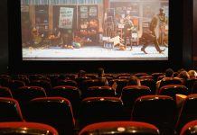 Biografsal med mennesker, der ser en animationsfilm på en stor skærm, med delvist fyldte røde sæder.