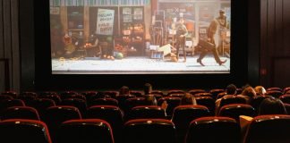 Biografsal med mennesker, der ser en animationsfilm på en stor skærm, med delvist fyldte røde sæder.