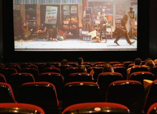 Biografsal med mennesker, der ser en animationsfilm på en stor skærm, med delvist fyldte røde sæder.