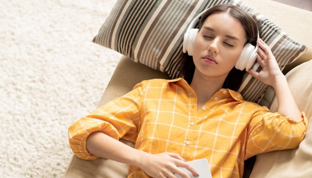Pige med hovedtelefoner ligger på en sofa og lytter til musik med lukkede øjne.