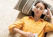 Pige med hovedtelefoner ligger på en sofa og lytter til musik med lukkede øjne.