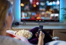 De 6 bedste streamingtjenester til din underholdning Kvinde ser TV med fjernbetjening og popcorn i hånden.