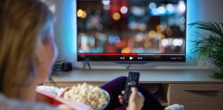 Kvinde ser TV med fjernbetjening og popcorn i hånden.