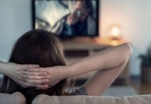 De 10 bedste streamingtjenester til dokumentarfilm En kvinde sidder på en sofa med hænderne bag hovedet og ser fjernsyn.