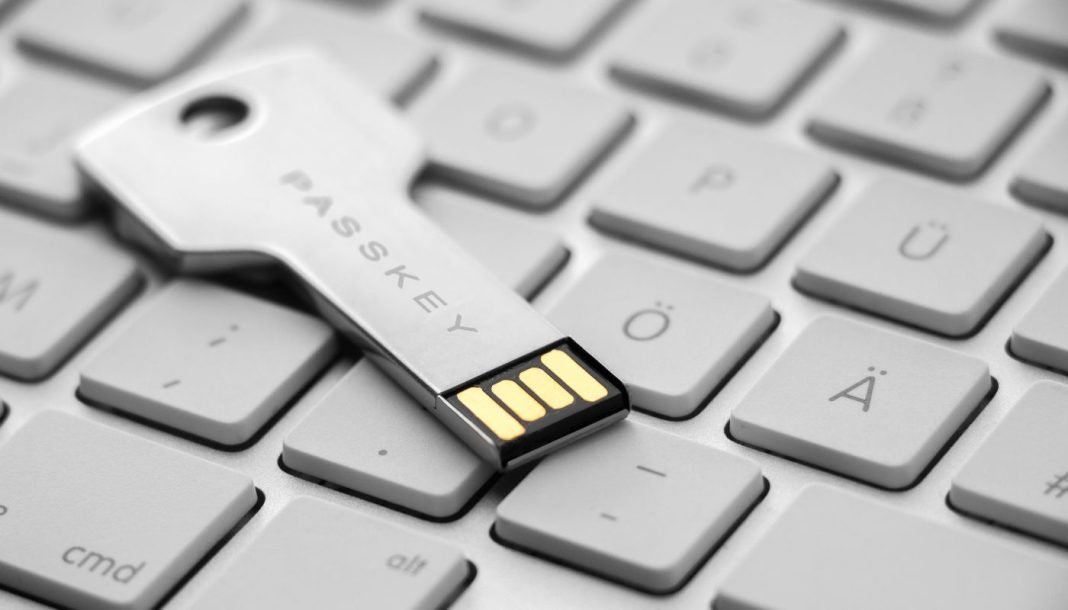 Et USB-drev i form af en nøgle med teksten "PASSKEY" indgraveret. Drevet ligger på et stilrent hvidt tastatur.