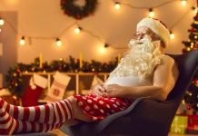 De 17 bedste julefilm at se på Disney+ En mand klædt ud som julemanden, der sidder afslappet i en stol. Han har en hvid tanktop, røde og hvide stribede sokker og røde shorts med hvide prikker.