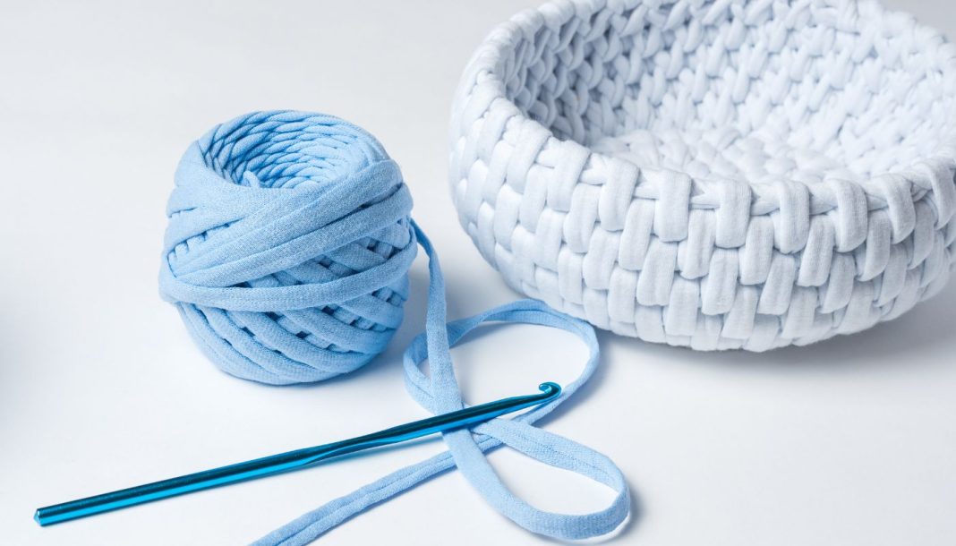 En hæklenål, et nøgle lyseblåt garn og en hæklet hvid kurv.