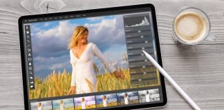 En tablet på et træbord ved siden af en kop kaffe. På tablettens skærm er et foto redigeringsprogram åbent, hvor et billede af en kvinde i en hvid kjole i en mark med høje græsstrå redigeres.