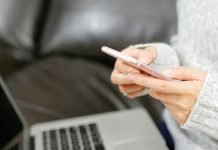 Person bruger en smartphone foran en bærbar computer i sofaen.