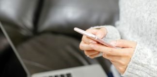 Person bruger en smartphone foran en bærbar computer i sofaen.