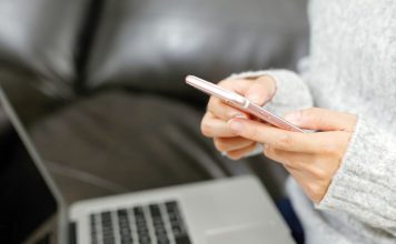 6 ting, du skal være opmærksom på, når du køber en brugt telefon Person bruger en smartphone foran en bærbar computer i sofaen.