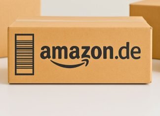 Amazon.de-pakken står centralt på et bord, omgivet af andre neutrale papkasser. Baggrunden er lys og enkel.